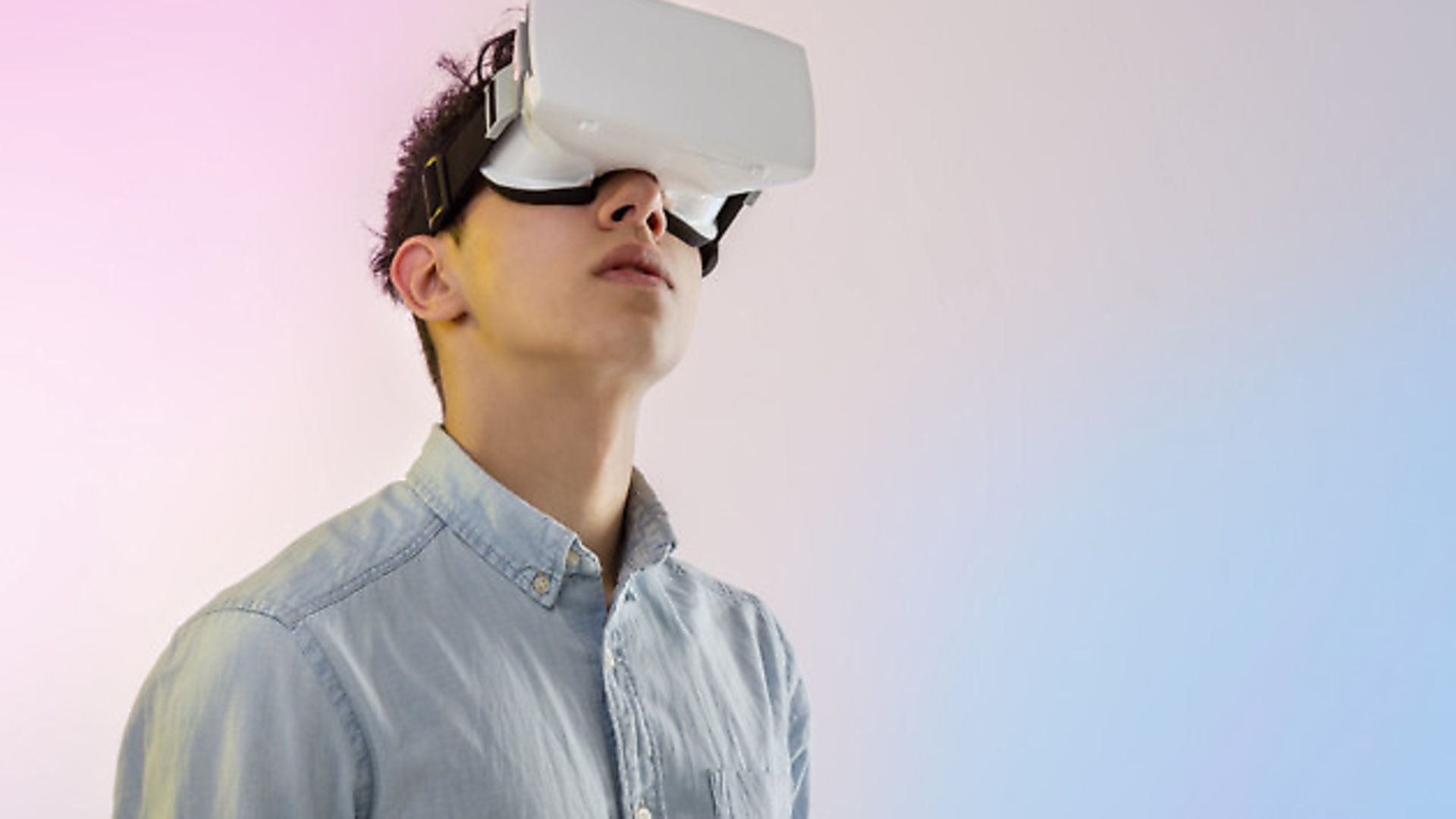 Young man wearing virtual reality headset looking up - Credit: Getty Images/Cultura RF