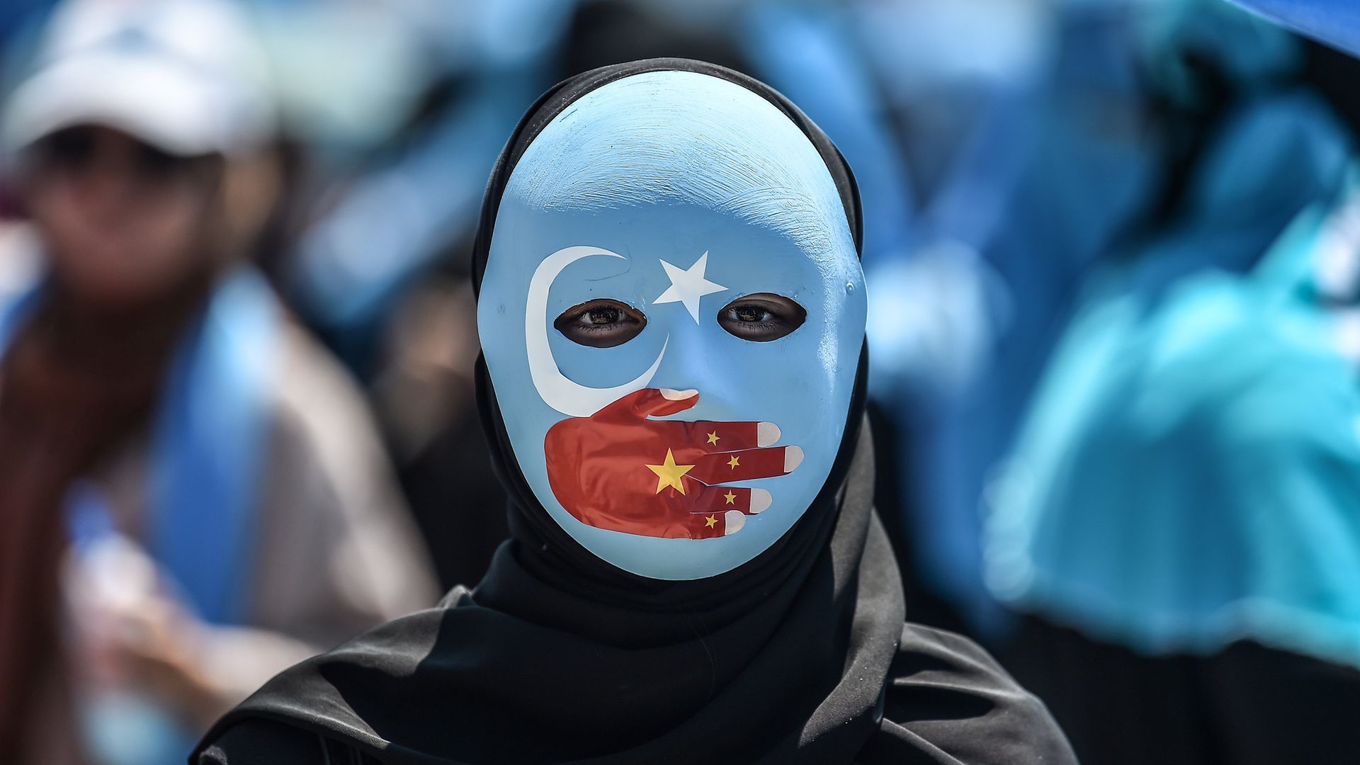 A demonstrator wearing a mask painted with the colours of the flag of East Turkestan and a hand bearing the colours of the Chinese flag attends a protest to denounce China's treatment of ethnic Uighur Muslims. - Credit: AFP via Getty Images
