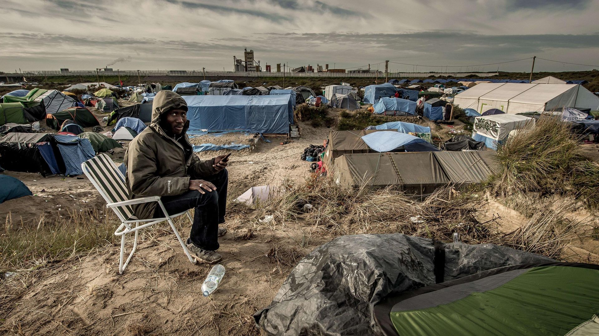 A Sudanese man looks on as he uses a phone to call his family in the "Jungle" migrants camp in Calais - Credit: PHILIPPE HUGUEN/AFP via Getty Images