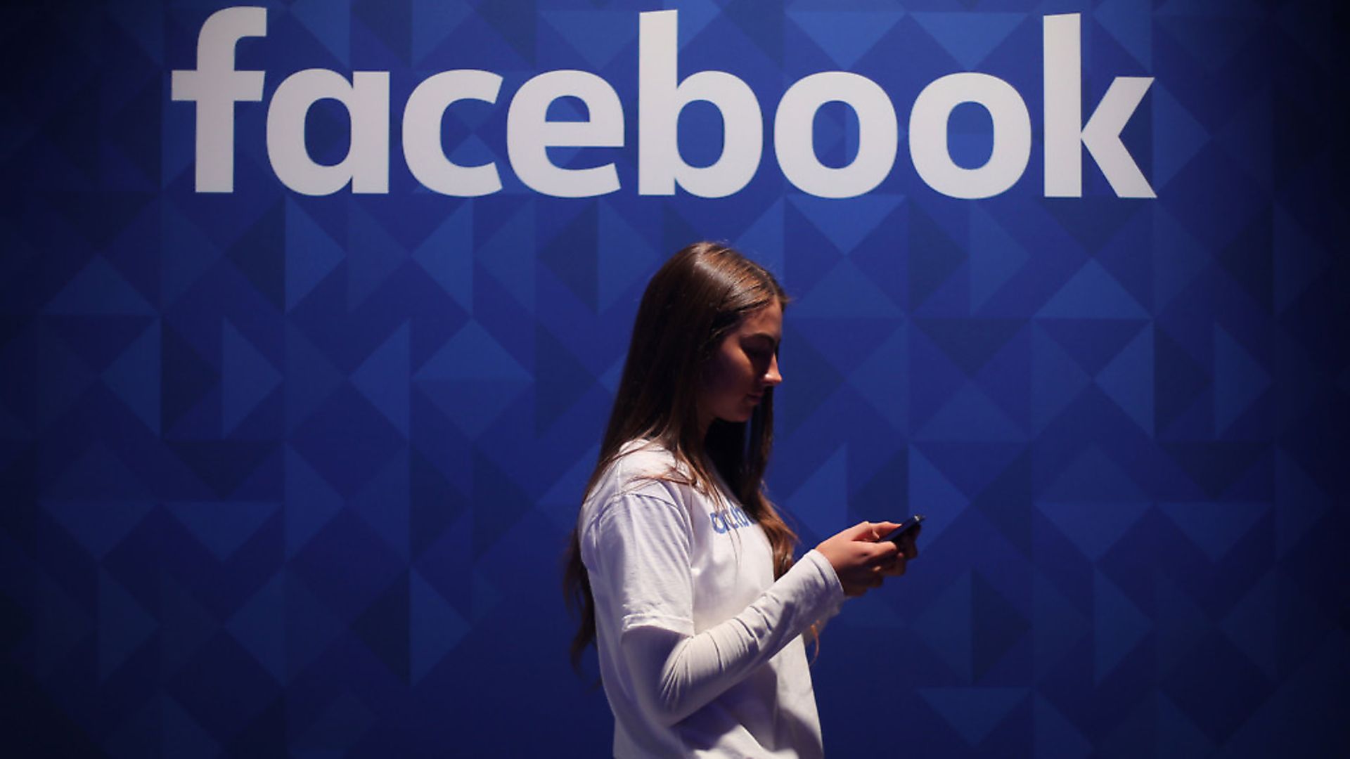 A woman using her phone under a Facebook logo. Photograph: Niall Carson/PA. - Credit: PA Wire/PA Images