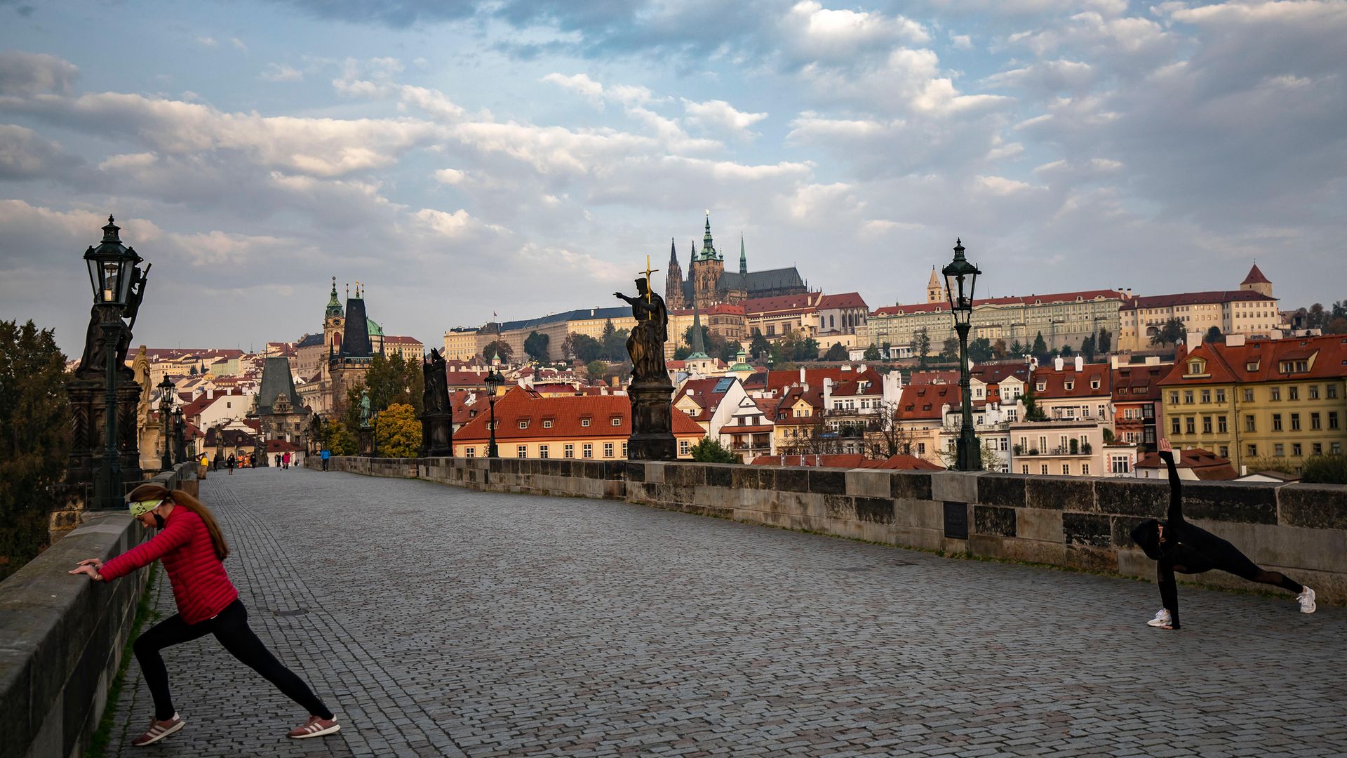 Two women stretch after a morning run on Prague's Charles Bridge, during the Czech Republic's partial coronavirus lockdown - Credit: Getty Images