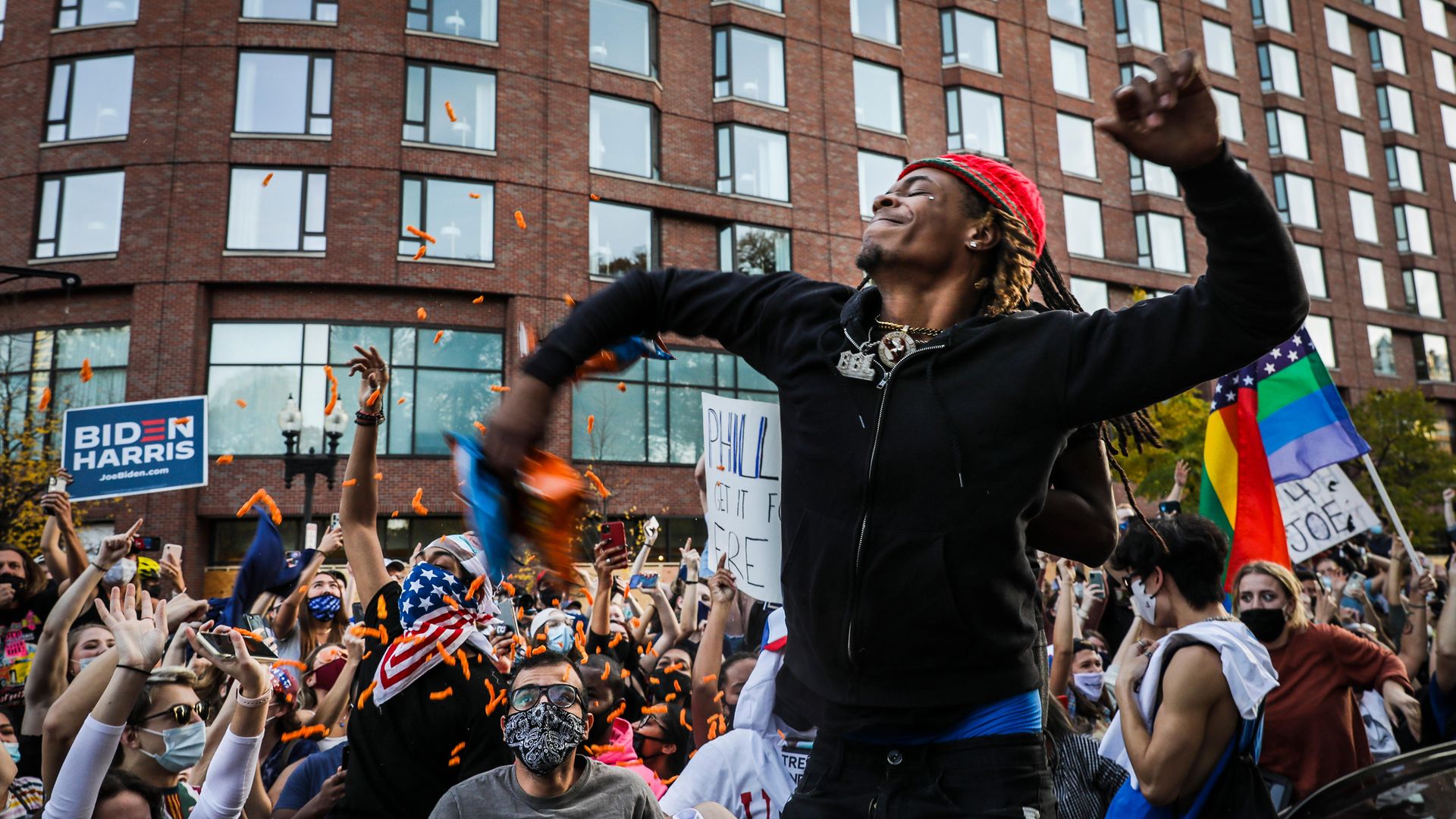 A man throws packs of crisps into a crowd amid jubilant celebrations in Boston of Joe Biden's election victory - Credit: Boston Globe via Getty Images