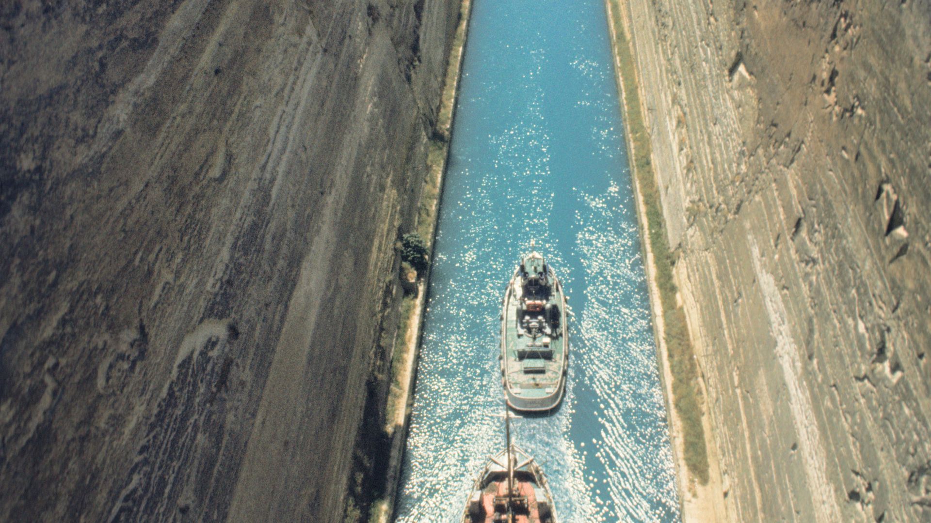 A tug boat and a larger vessel pass along the Corinth canal, in Greece - Credit: Universal Images Group via Getty