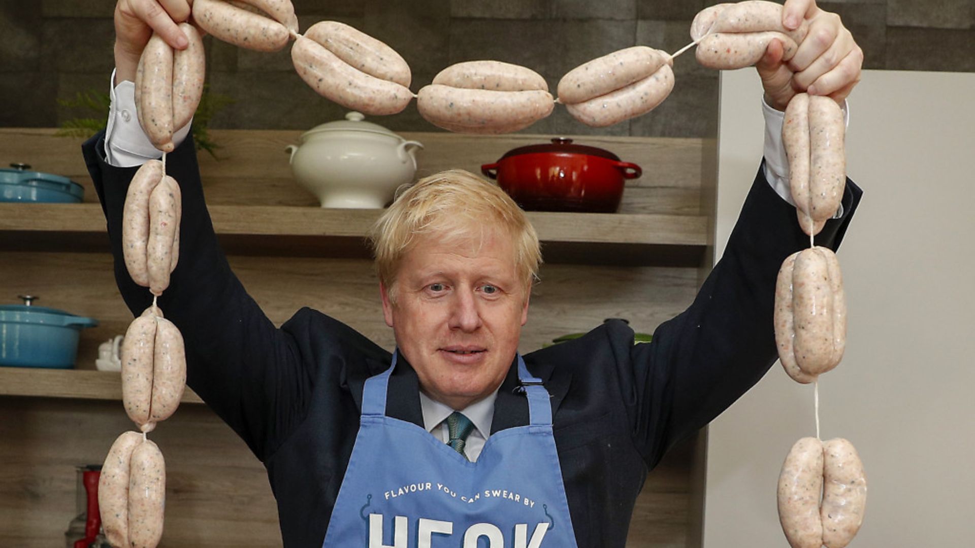 Boris Johnson holds up a string of sausages around his neck - Credit: PA