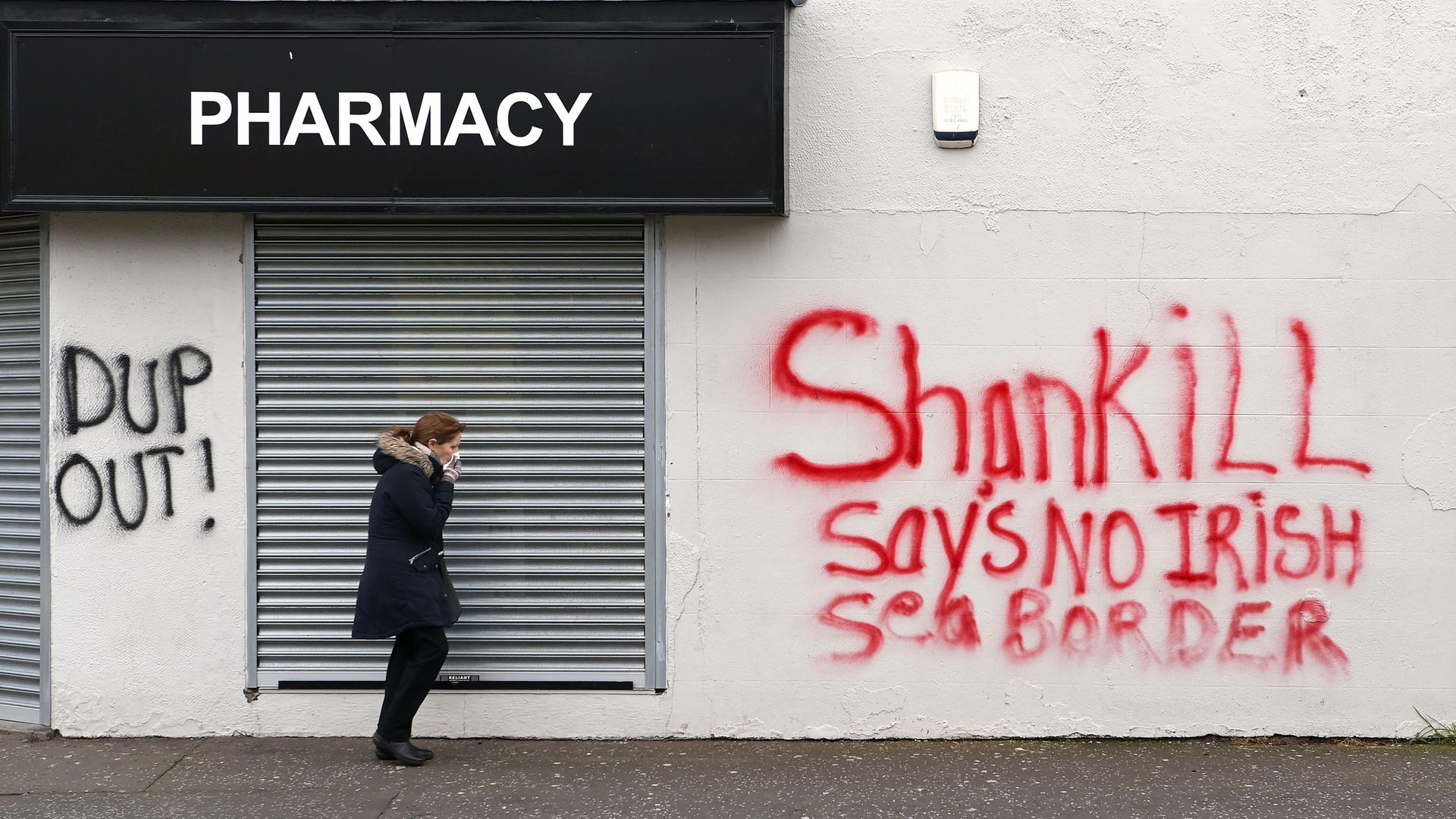 A woman walks past freshly painted loyalist graffiti in the Shankill area of Belfast, Northern Ireland - Credit: Getty Images