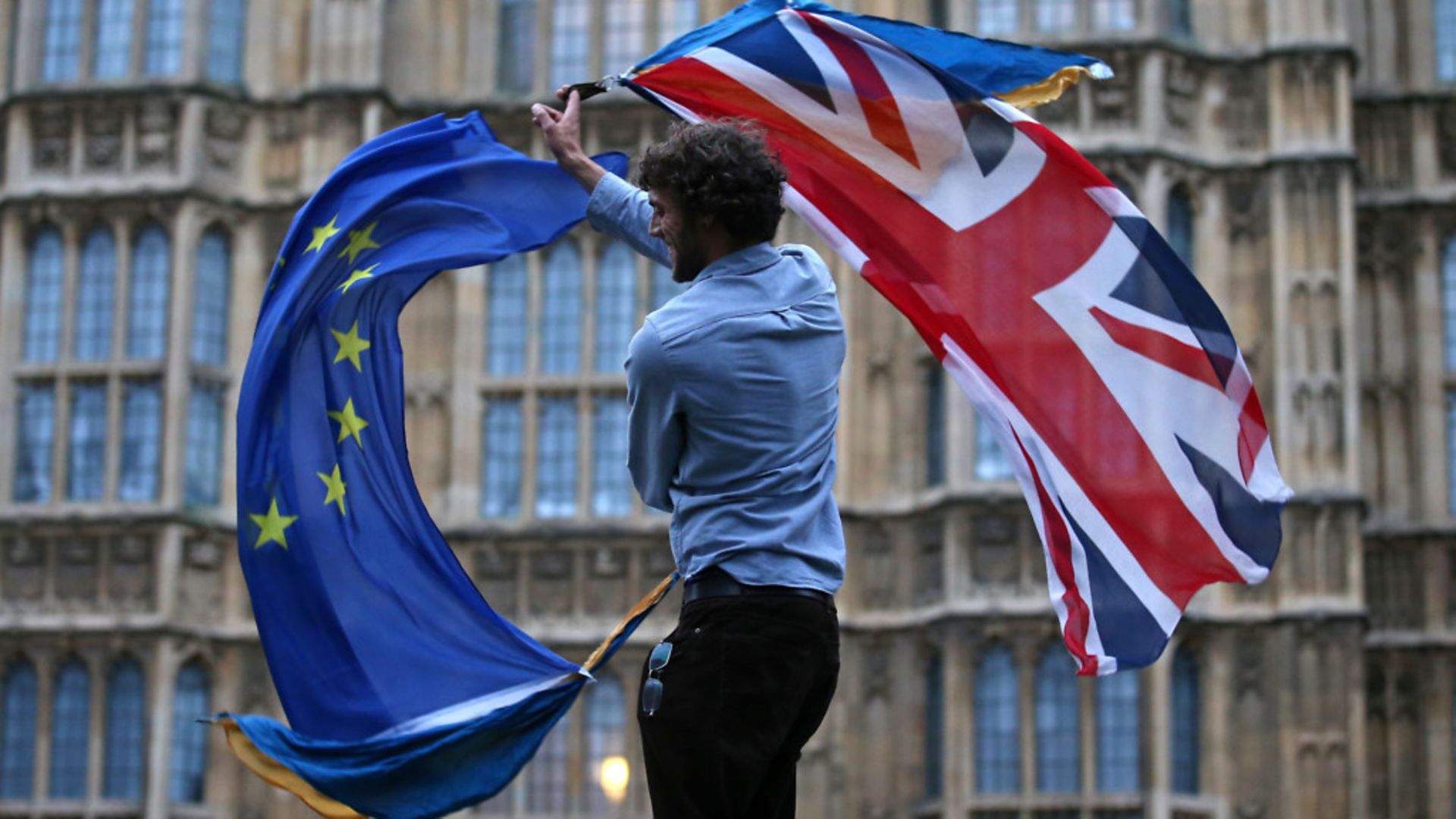 A man waves both a Union flag and a European flag together on College Green outside the Houses of Parliament - Credit: AFP via Getty Images