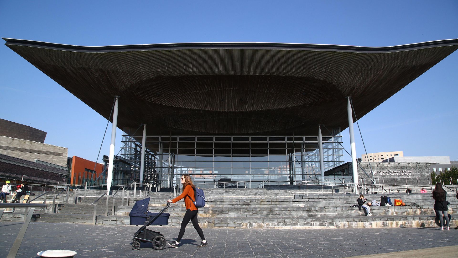 A woman pushes a pram past the senedd building in Cardiff Bay - Credit: AFP via Getty Images