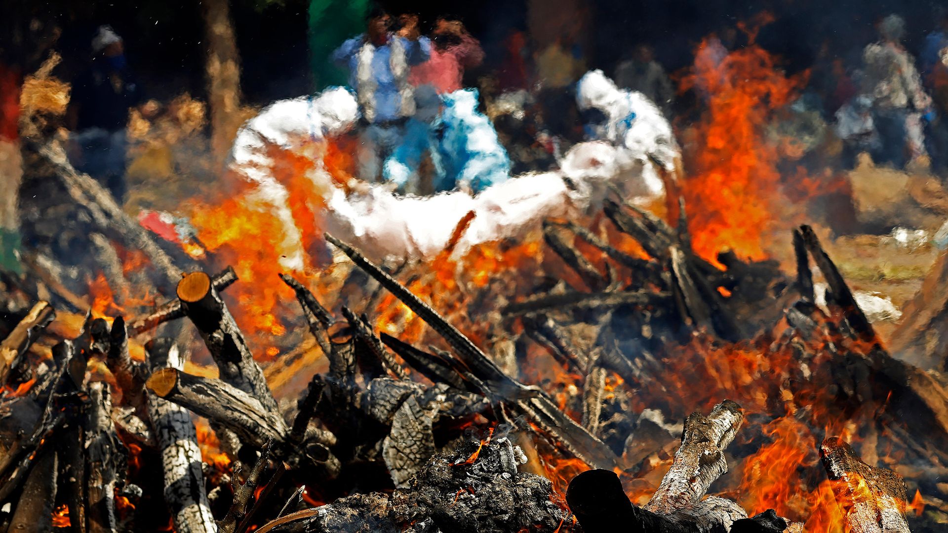 Undertakers wearing protective suits carry a body next to a burning pyre of a Covid victims in Delhi - Credit: SOPA Images/LightRocket via Gett