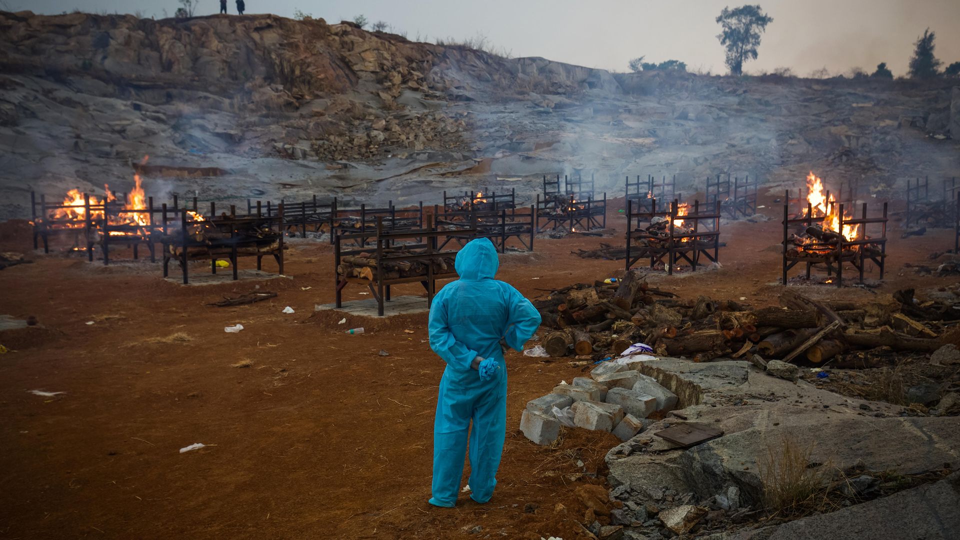 A man watches mass cremations in a disused granite quarry repurposed to cremate those who have died from Covid in Bengaluru, India - Credit: Getty Images