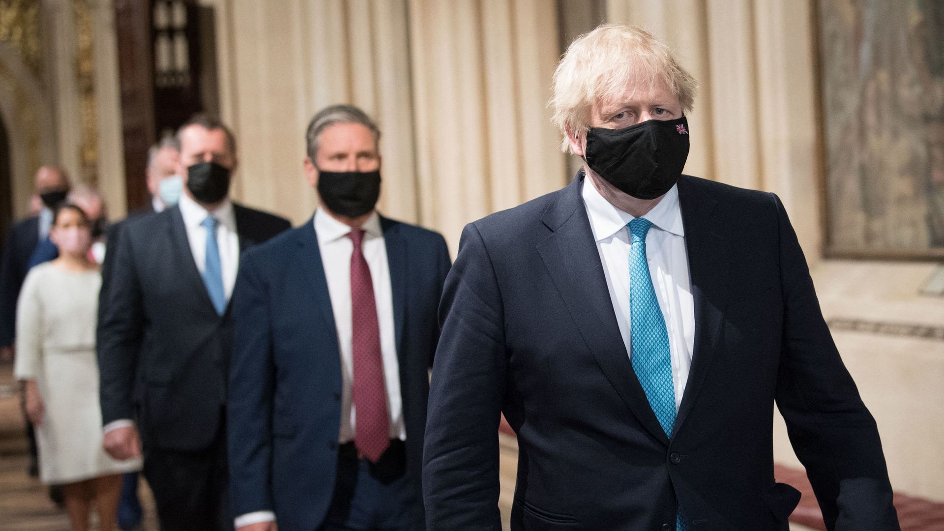 Prime Minister Boris Johnson (R) and opposition leader Keir Starmer (C), both wearing face coverings, walk in a socially distanced single file line through the Central Lobby after listening to the Queen's Speech - Credit: POOL/AFP via Getty Images