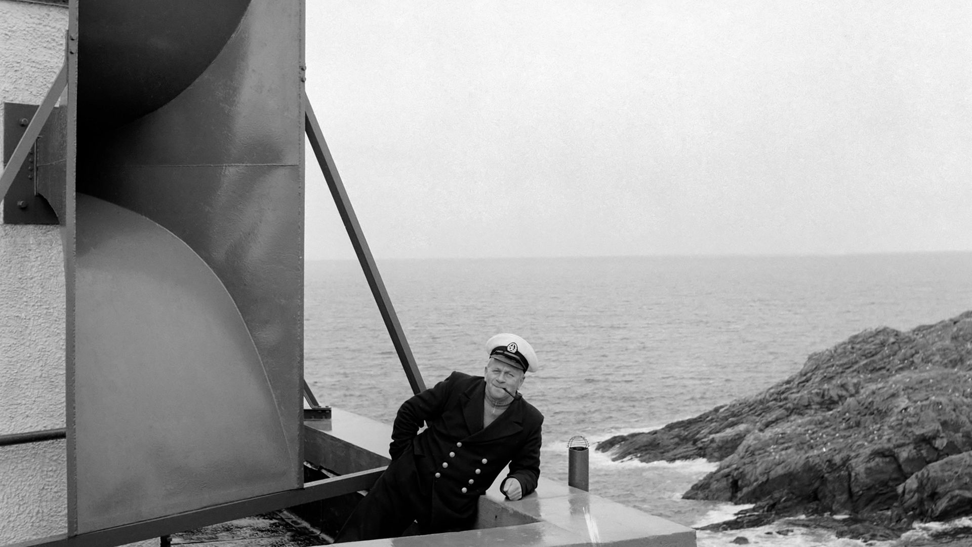 A lighthouse keeper at Strathy Point, on the north coast of Scotland, poses in front of the site's vast foghorn, in 1960 - Credit: Mirrorpix via Getty Images