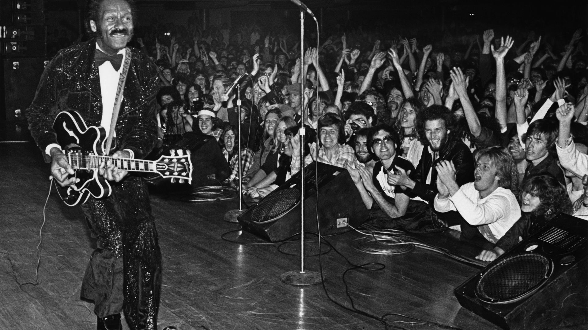 Chuck Berry struts his signature "duck walk" while playing his Gibson guitar, to the delight of fans, during a 1980 Hollywood, California, concert at the Palladium - Credit: Getty Images