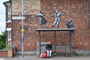 A man and his shopping at a bus stop in Great Yarmouth, below Banksy’s graffiti artwork of a couple dancing to an accordion player. Photo: Justin Tallis/AFP via Getty Images.