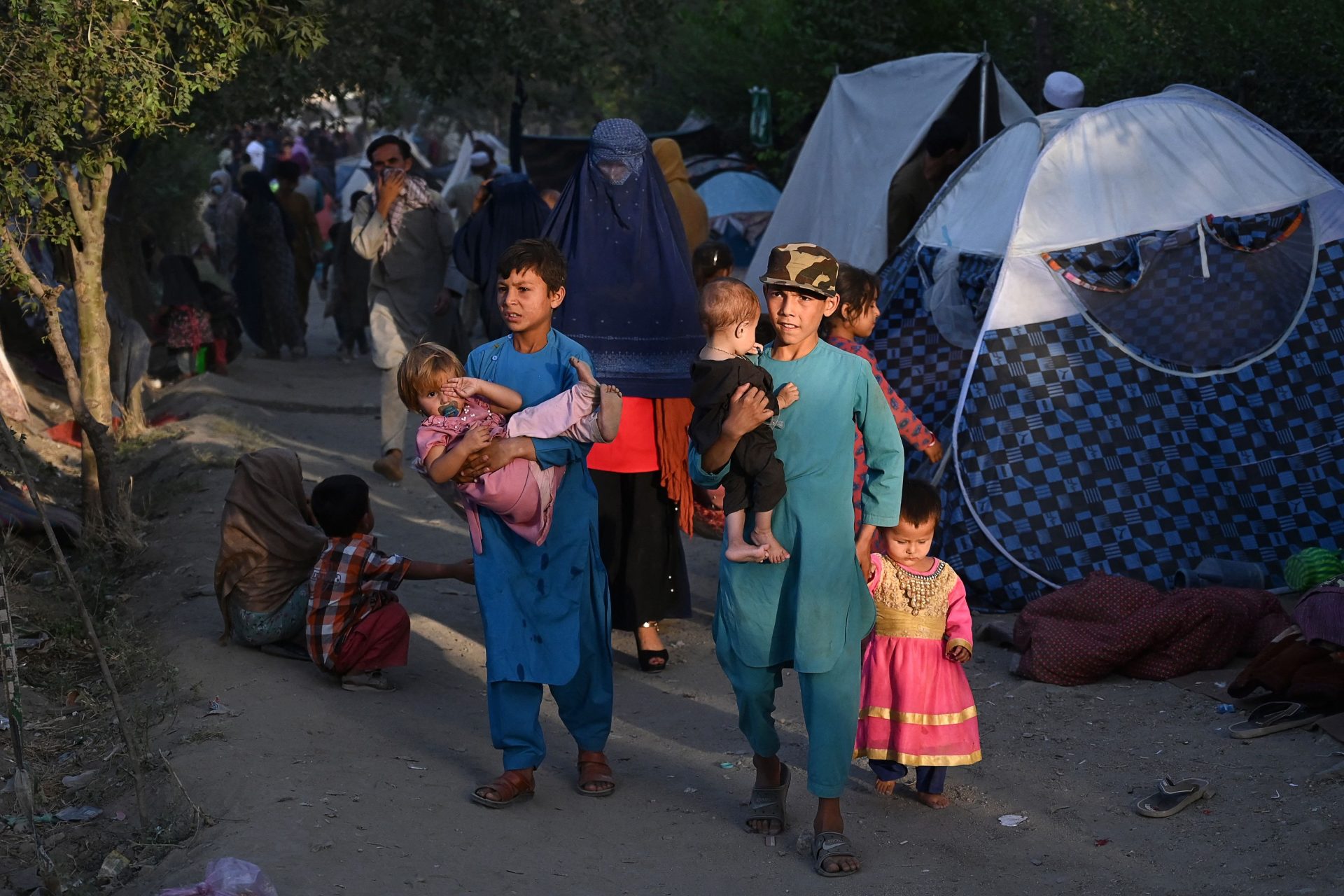 Displaced Afghan families, who fled from Kunduz, Takhar and Baghlan province as the Taliban approached, walk past their temporary tents at Sara-e-Shamali in Kabul on August 11. Photo: Wakil Kohsar/AFP via Getty Images.