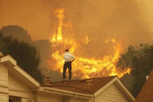 A man on a rooftop in Camarillo looks at approaching flames as wildfires sweep California in 2013. Nearly 10,000 fires burned through 601,625 acres (2,434.69 km2) of land in the state that year. Photo: David McNew/Getty Images.