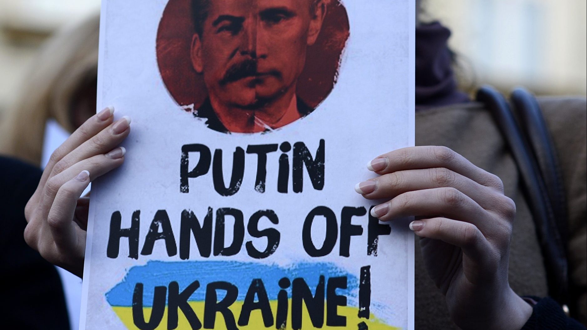 A woman holds a placard reading "Putin, hands off Ukraine" depicting a collage of Russian President Vladimir Putin and Soviet leader Josef Stalin. Photo:MICHAL CIZEK/AFP via Getty Images