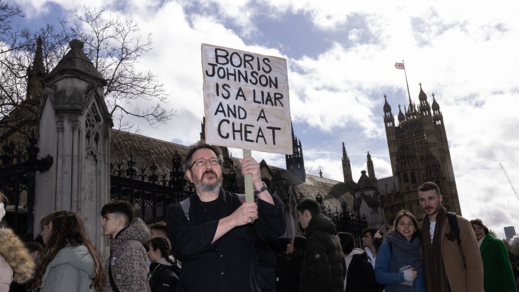 A protester holds a sign outside parliament as Boris Johnson gives evidence to the Privileges Committee on March 22. Photo: Dan Kitwood/Getty
