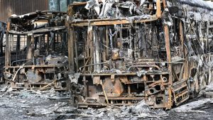 Burnt buses seen through the gates at the Fort d'Aubervilliers bus terminal in front of the future Paris 2024 Olympic swimming venue (Photo by BERTRAND GUAY/AFP via Getty Images)