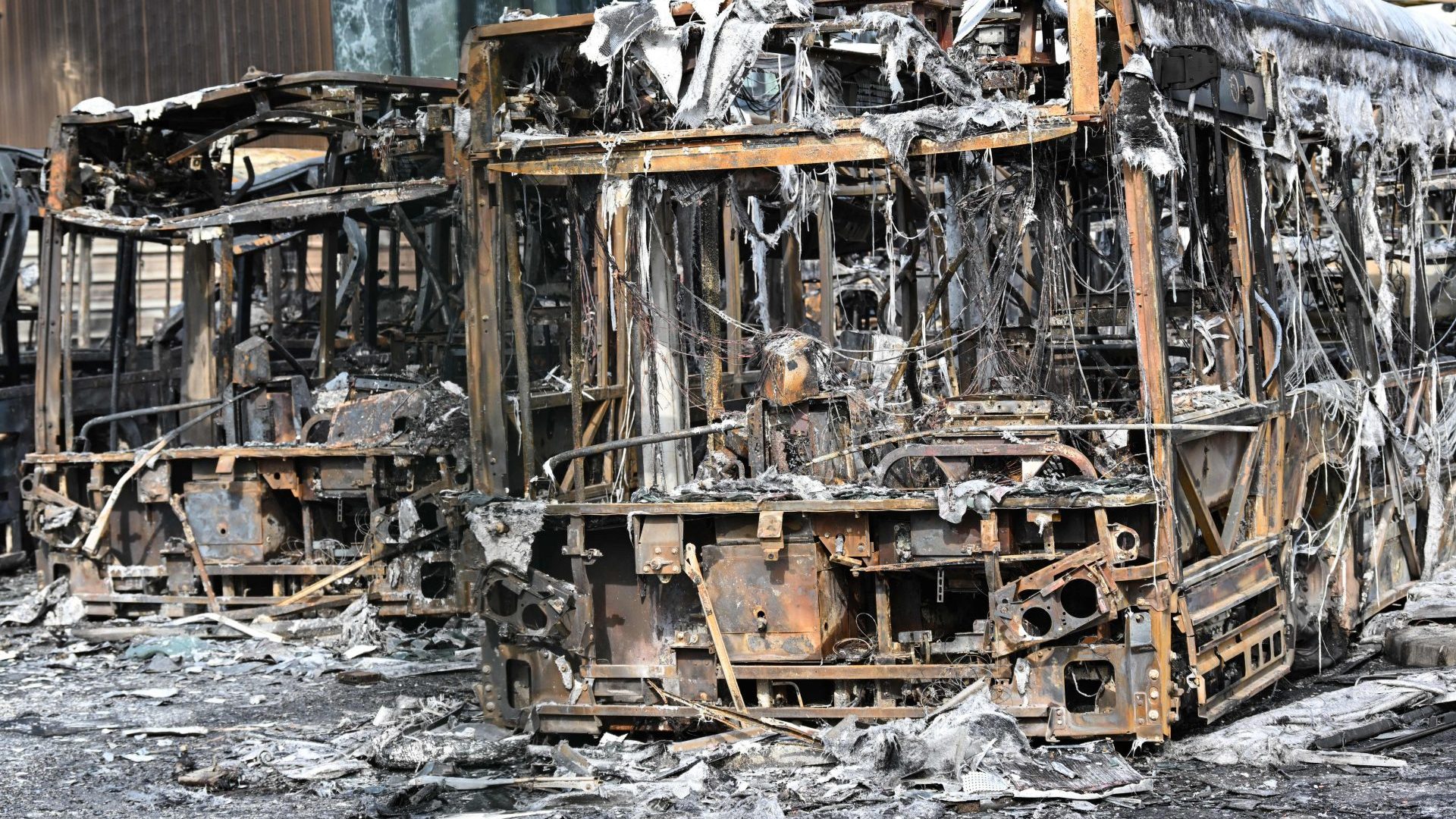 Burnt buses seen through the gates at the Fort d'Aubervilliers bus terminal in front of the future Paris 2024 Olympic swimming venue (Photo by BERTRAND GUAY/AFP via Getty Images)