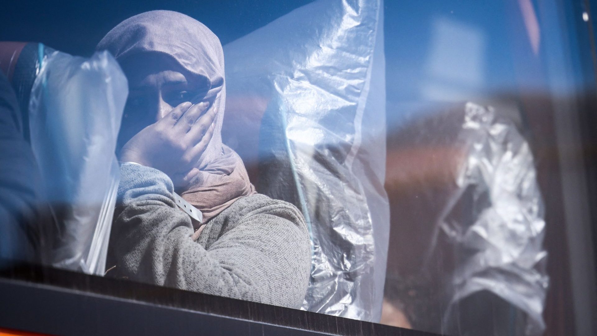 A migrant woman looks out from the window of a bus that will take her and other migrants for processing, in Dungeness. Photo: HENRY NICHOLLS/AFP via Getty Images