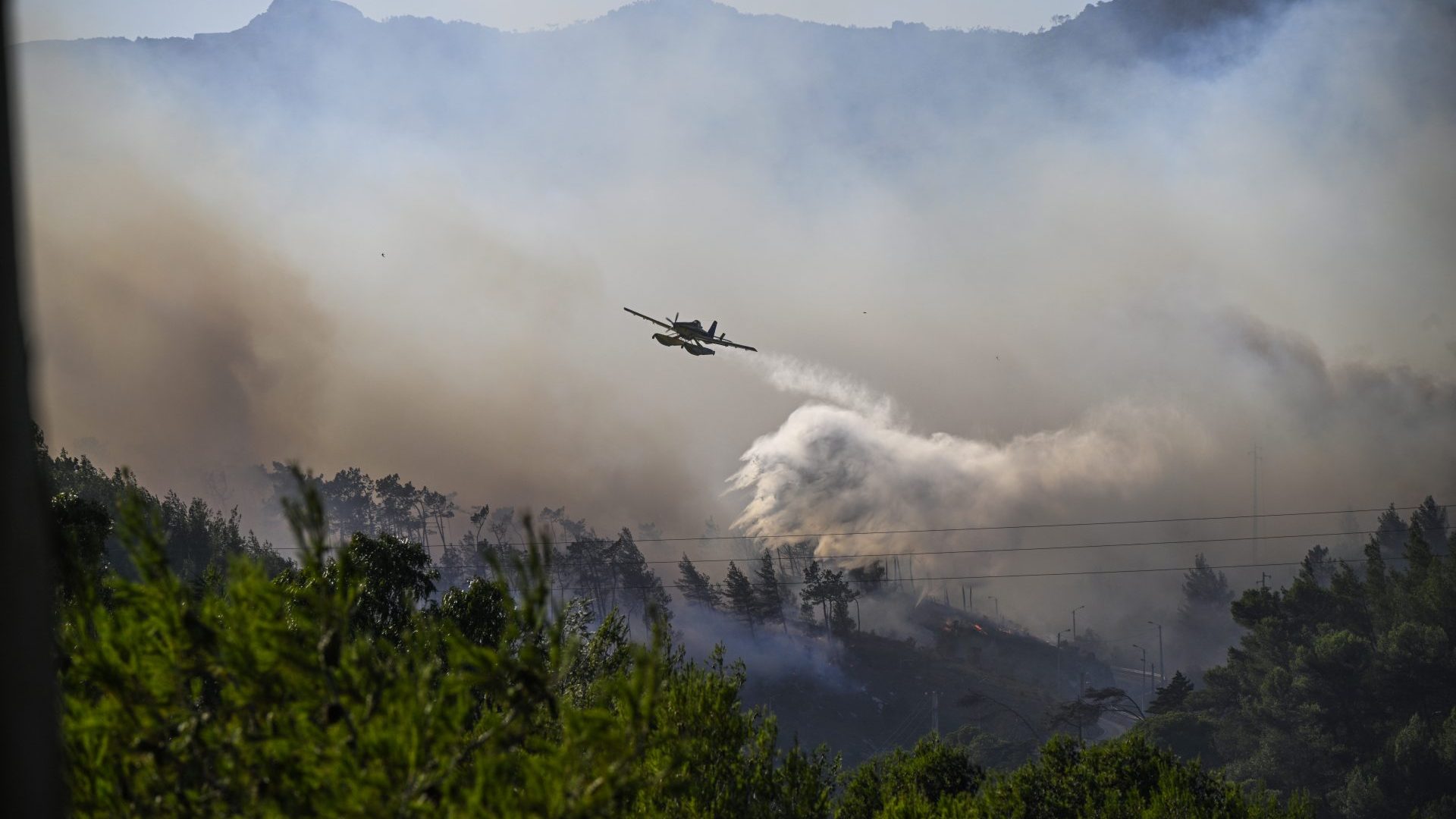 An AT-802F Fire Boss firefighting amphibious aircraft flies over heavy smoke to drop water at a forest fire in Cascais, west of Lisbon. Photo: De Melo Moreira/AFP