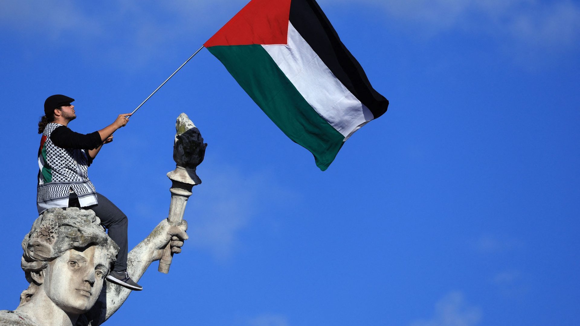 A protester sitting on the Le Triomphe de la République statue in Paris waves a Palestinian flag during a demonstration calling for peace in Gaza. Photo: Emmanuel Dunand/AFP/Getty