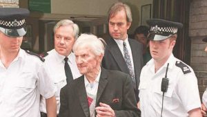 Szymon Serafinowicz (C) is escorted by policemen from the Epsom magistrates court 13 July after he was charged with the murder of four Jews in the years 1941 and 1942 in villages in Nazi occupied Bielorussia where he was alledgedly local police chief. Photo: JOHNNY EGGITT/AFP via Getty Images