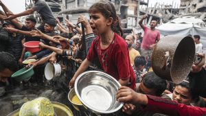 Displaced Palestinians crowd with outstretched hands and containers to receive hot meals distributed by aid organizations at the Jabalia Refugee Camp in northern Gaza City. Photo: Mahmoud Issa/Anadolu via Getty Images